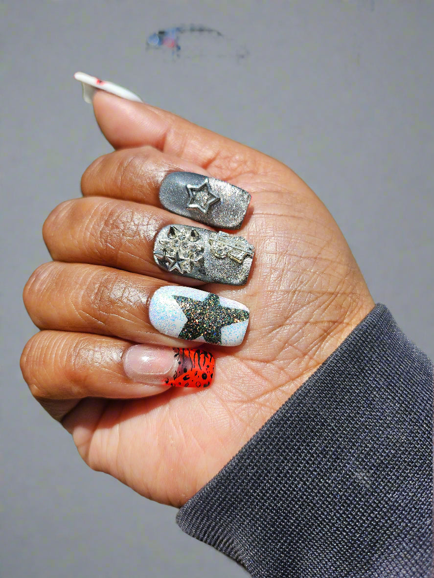 Close-up of a hand with intricately designed nails, outdoors.
